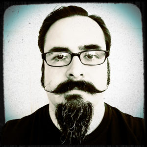 Portrait photograph of Sebastian Aravena with a long curly mustache and a long pointy beard with short tightly parted hair. Selfie photograph by Sebastian Aravena.