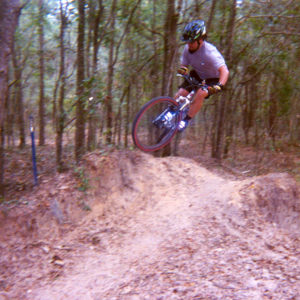 Mountain biking photograph of Sebastian Aravena doing a whip on a small jump at The Vortex section of the Santos Trail system in Belleview, Florida. Photograph by Paul Scusa.